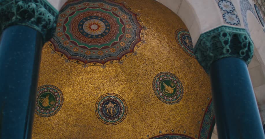An ornate golden mosaic ceiling with intricate Islamic patterns is revealed from between marble pillars