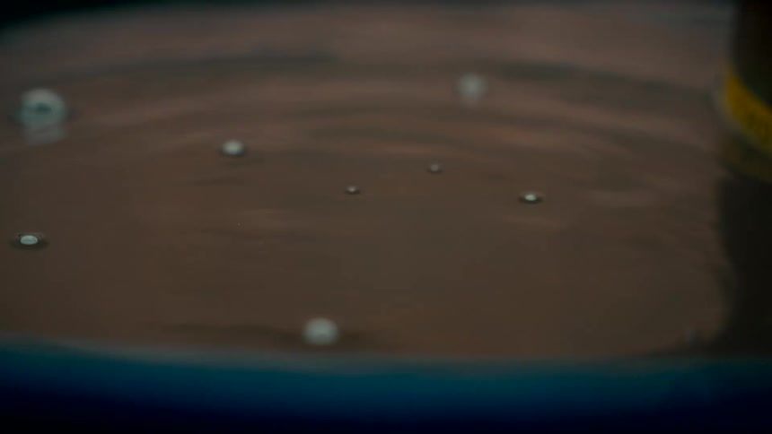 A macro shot in super slow motion of a single water droplet falling into a calm pool of water, creating a crown splash and concentric ripples