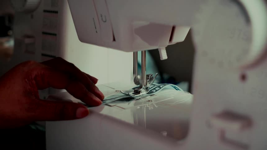 A close-up shot of a person's hand guiding patterned fabric through a modern sewing machine