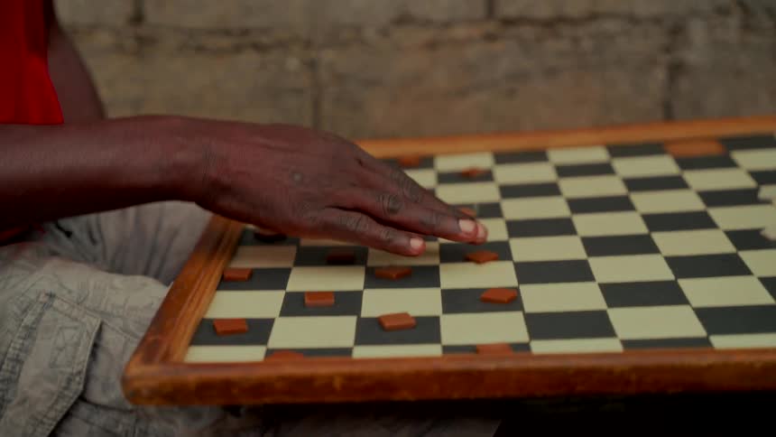 A close-up slow pan shows a man's hand as he thoughtfully considers his next move in a game of checkers