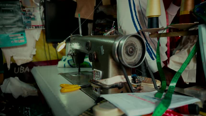 An old industrial sewing machine works continuously in a cluttered tailor's workshop