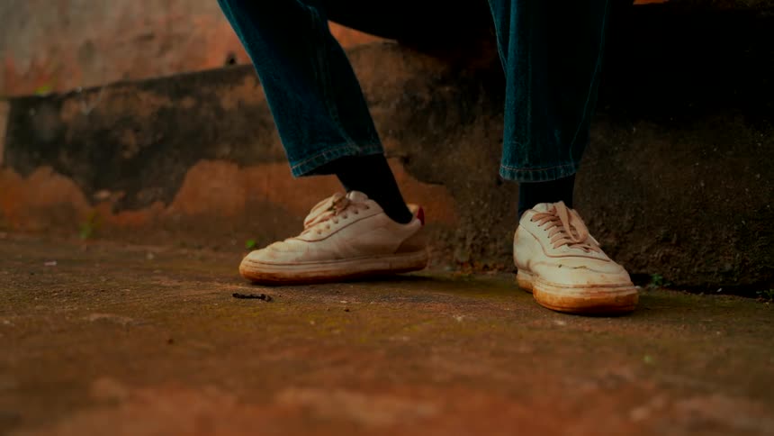 Close-up shot of a person's dirty white sneakers as they sit still on a concrete step