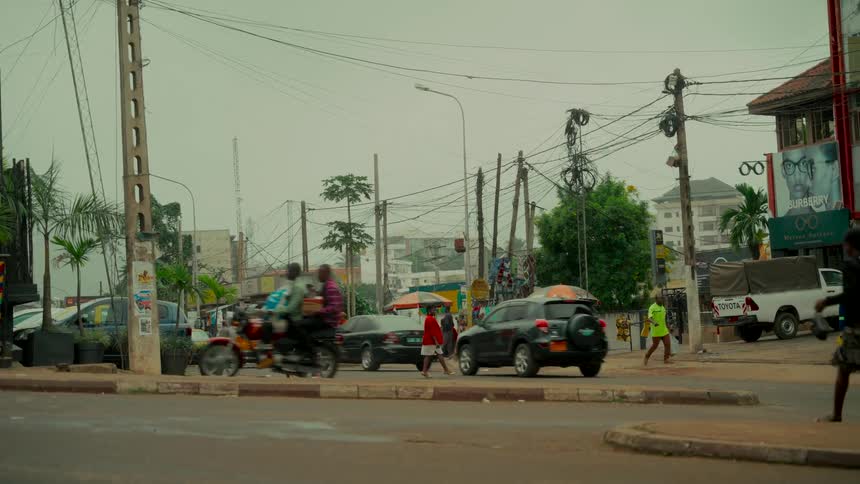 Slow motion captures the daily hustle of a busy street corner in Africa, with cars, motorcycles, and pedestrians navigating the intersection