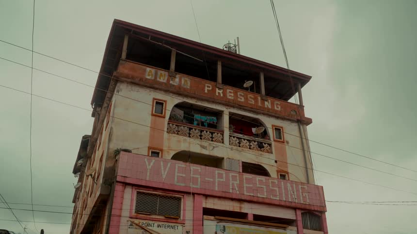 A static, low-angle shot of a weathered pink and white building with a laundry business under an overcast sky