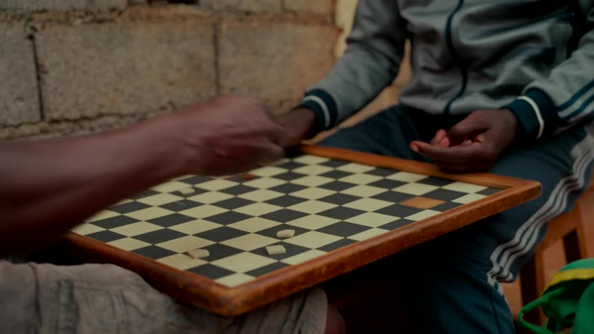 A close-up of two men's hands engaged in a fast-paced game of checkers outdoors in a rustic setting