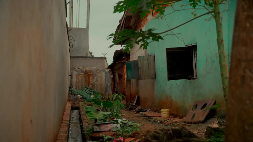A static wide shot of a dirty, narrow alleyway between rundown buildings in a slum on an overcast day