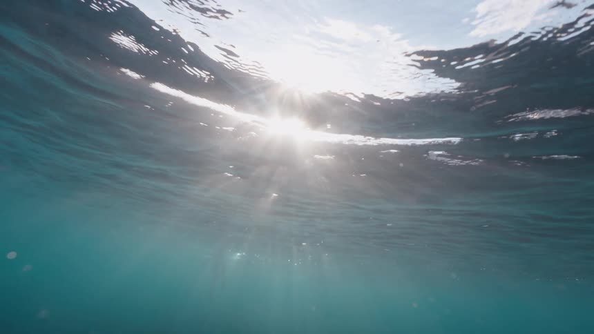 Sunbeams gracefully pierce through the gentle ripples of the ocean surface in a serene underwater view