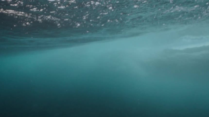 An immersive underwater view in slow motion as a powerful wave passes overhead, revealing the calm, deep ocean below