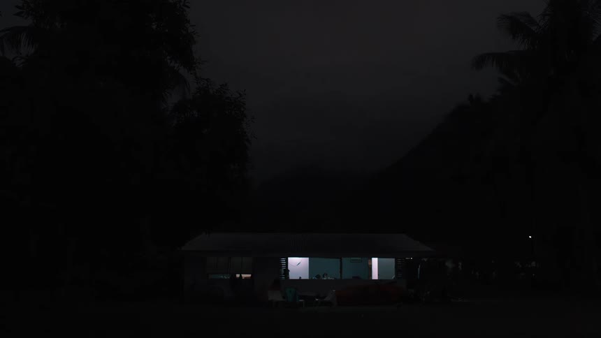 A tilting shot reveals a house with lights on at night, nestled amongst dark trees and mountains