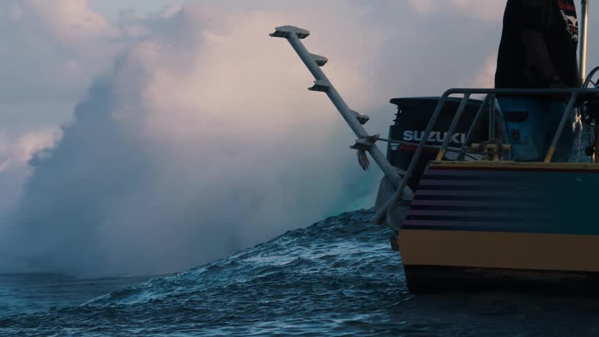 A massive ocean wave crashes in dramatic slow motion as seen from the back of a boat at sea