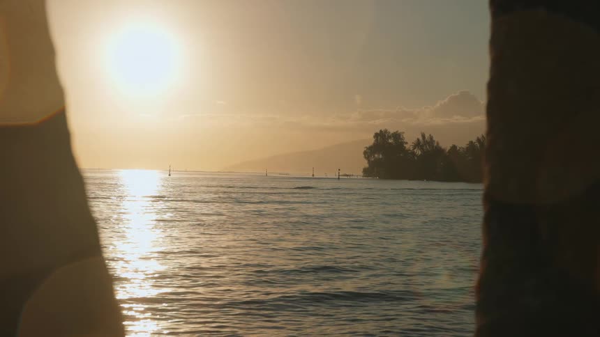 A serene golden sunset over the ocean is framed between two silhouettes on a tropical island