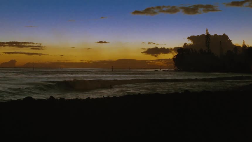 A gentle wave rolls towards the shore in slow motion during a picturesque twilight sunset over the ocean
