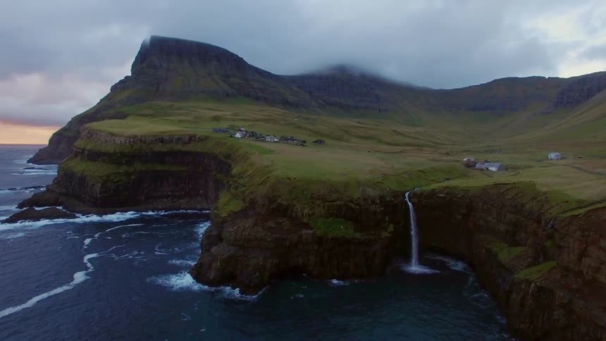 A waterfall near a small village flows over a cliff to the ocean below