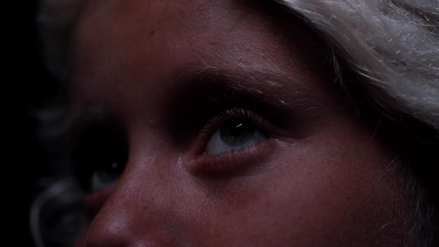 An extreme close-up shot of an eye with blonde hair looking around in a moody, dark environment