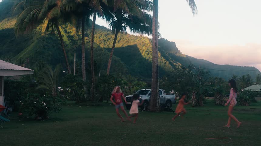 Slow motion of several young girls playing jump rope together in a yard with a beautiful tropical mountain backdrop