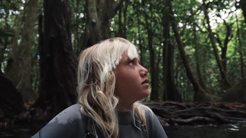A young adventurer in a wetsuit gazes up in wonder at the lush, green jungle canopy while floating in a serene river