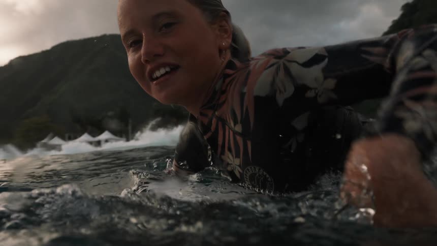 A smiling female surfer holds a friend's hand before paddling out on her board in a beautiful tropical ocean in cinematic slow motion