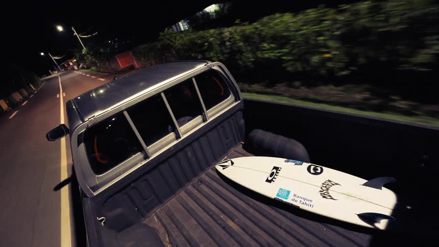 A high-angle time-lapse from the back of a pickup truck reveals a surfboard in the bed while driving down a dimly lit road at night