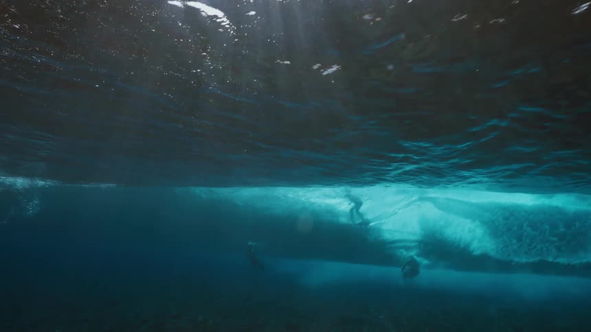 A unique underwater perspective captures a surfer in slow motion gliding across a powerful ocean wave as sun rays shine through the water