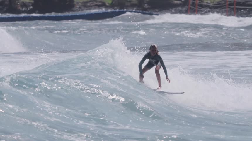 In slow motion, a young surfer expertly navigates a powerful ocean wave, performing a stylish cutback on the foamy crest