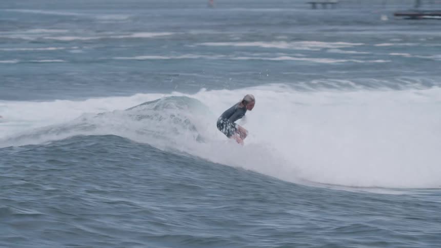 A talented young female surfer in a wetsuit skillfully rides a long breaking wave in slow motion