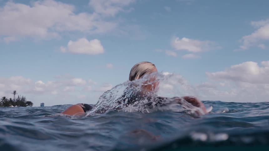 A female surfer paddles on her board in the ocean, captured in a beautiful slow-motion, half-underwater shot