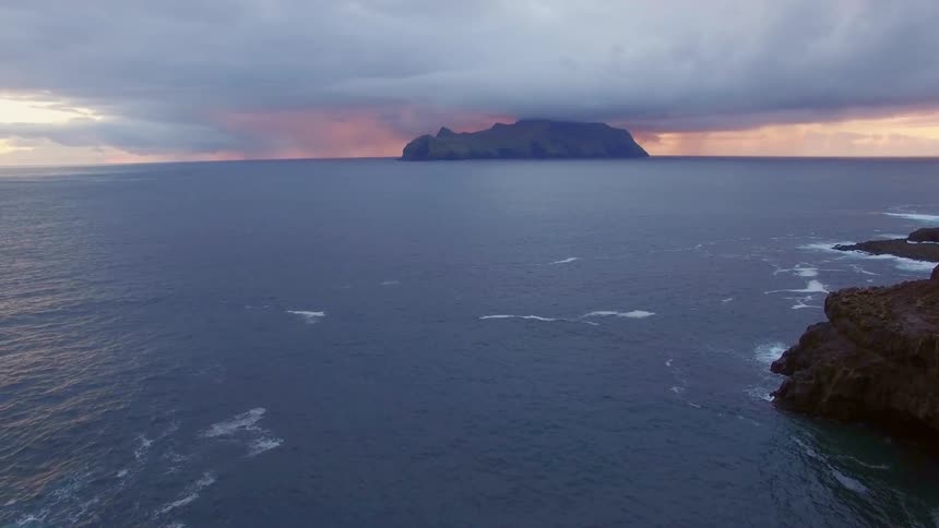 A person sits on a bluff looking out over the ocean