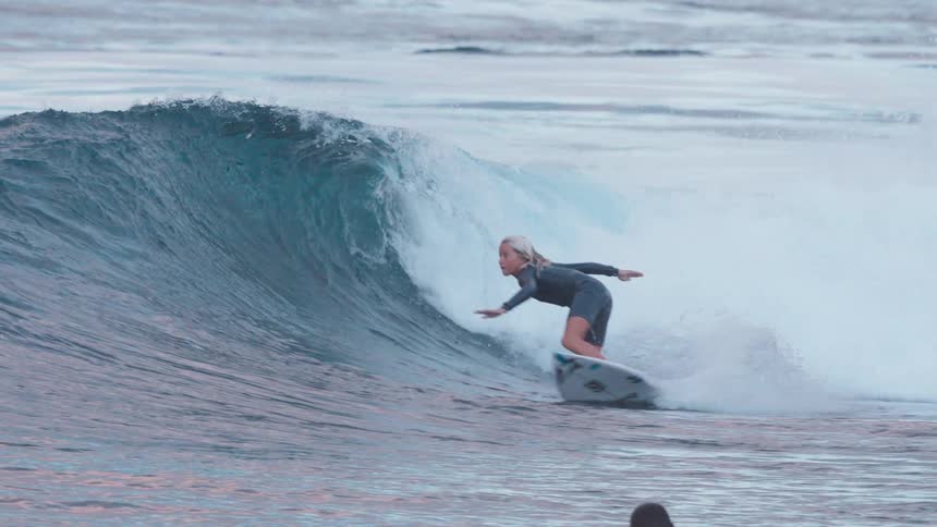 A talented young blonde surfer expertly catches a wave and performs a dramatic turn on the crest in super slow motion