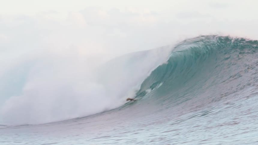 An enormous, perfectly formed ocean wave barrels in slow motion, catching a surfer inside its powerful curl