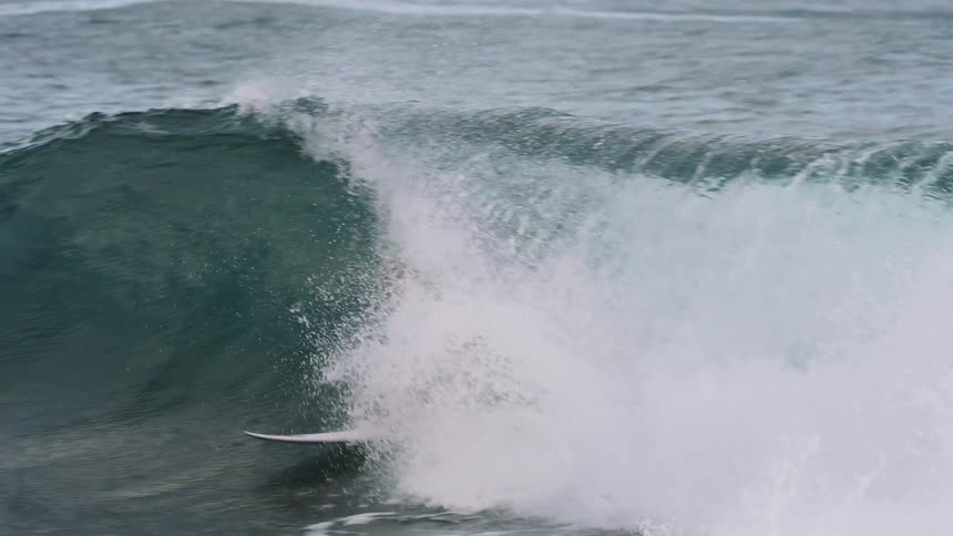 A skilled female surfer expertly rides inside the barrel of a powerful ocean wave in dramatic slow motion