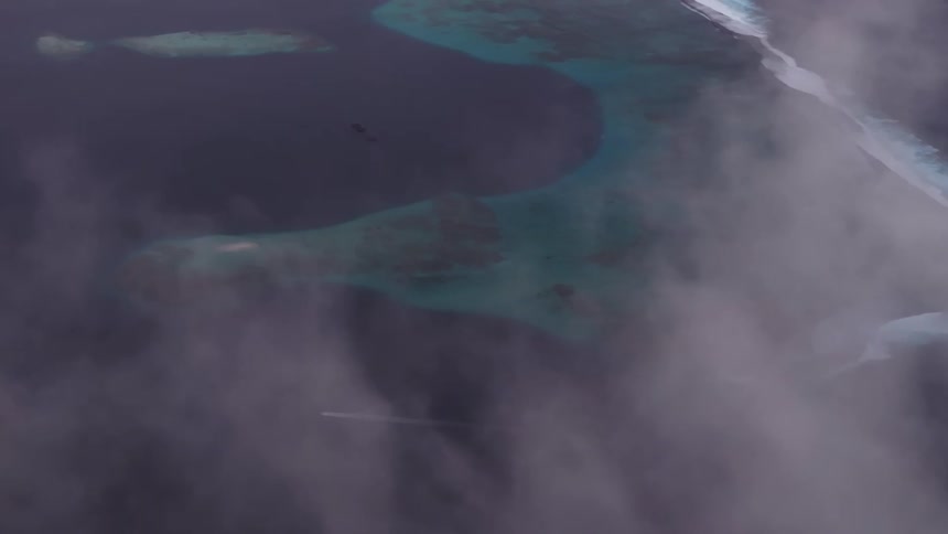 A mesmerizing aerial view flying through clouds reveals the stunning coastline of a tropical island with turquoise waters