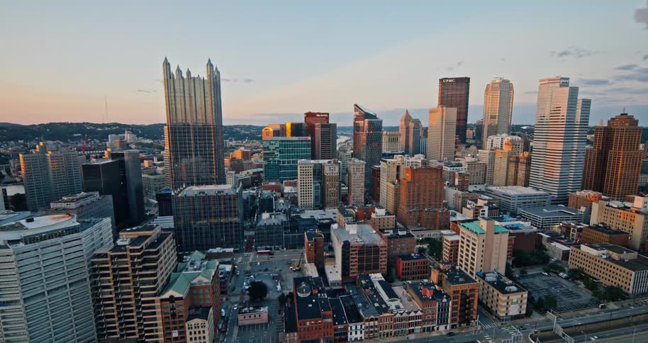 A slow push-in aerial shot captures the Pittsburgh, Pennsylvania skyline illuminated by the warm light of a beautiful sunset