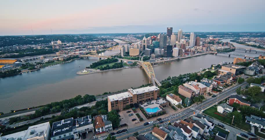A beautiful ascending aerial view of the Pittsburgh, Pennsylvania city skyline and its iconic yellow bridges over the river at twilight