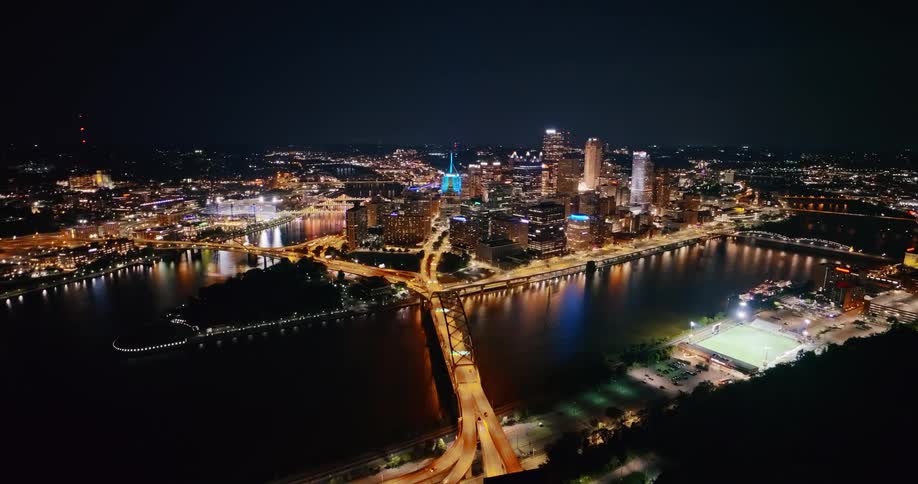 A stunning aerial view of a vibrant city skyline at night, with illuminated skyscrapers reflecting in the river and traffic moving across the bridges