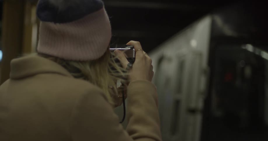 A woman takes pictures of subway trains passing by at night