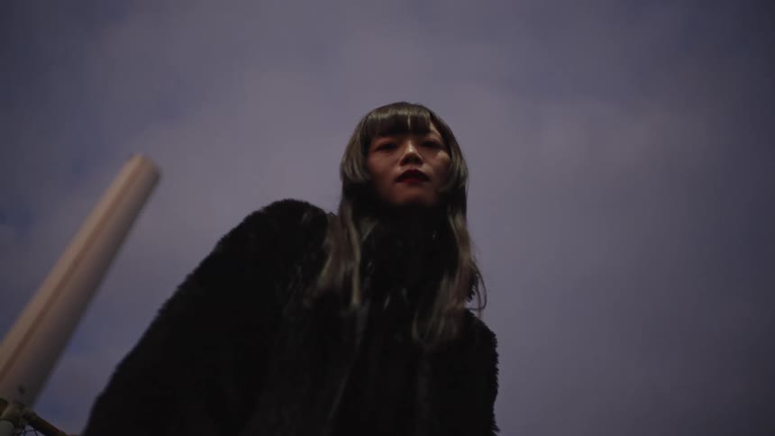 A woman with an intense gaze stares down at the camera in slow motion against a moody evening sky