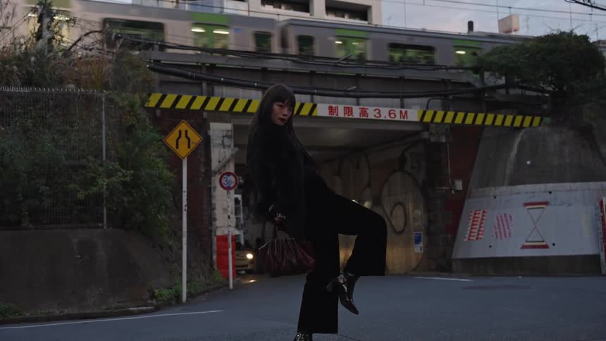 A fashionable woman strikes a pose on an urban street in Tokyo as a train passes on the overpass behind her