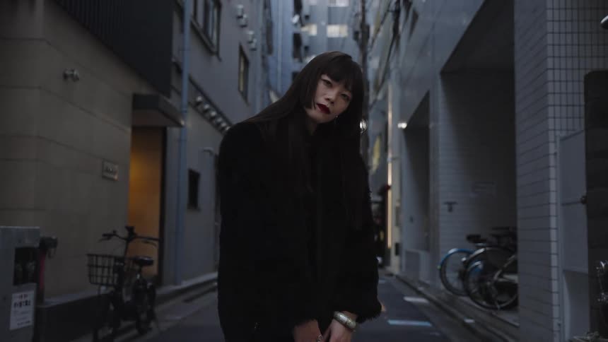 An enigmatic figure dressed in black slowly comes into focus and delivers an intense stare in a dark city alley
