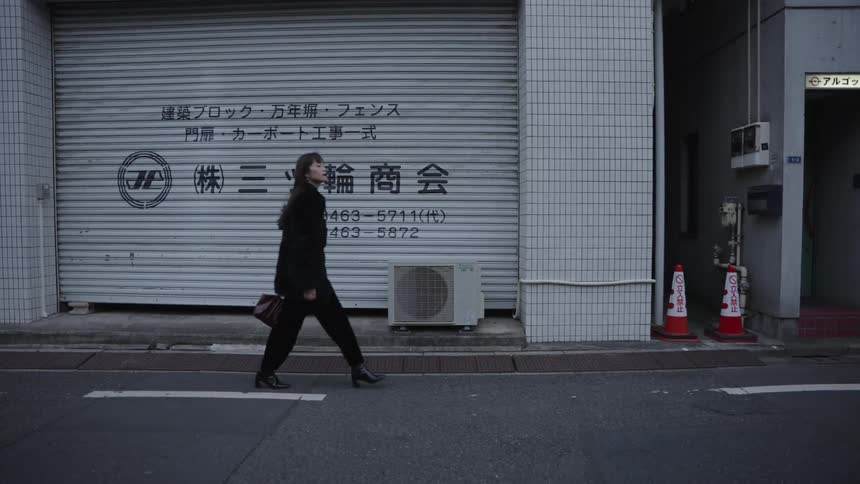 Slow motion shot of a stylish woman in black walking down a quiet urban street in Japan