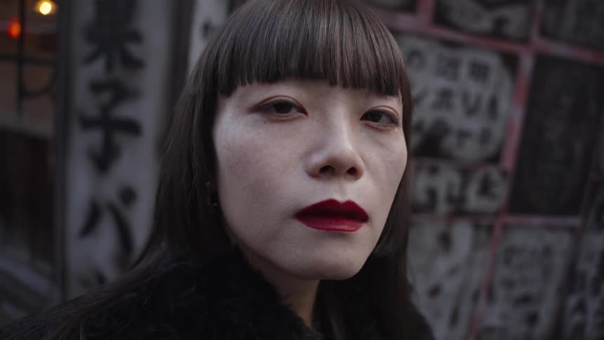 An intense close-up portrait of a stylish East Asian woman with red lipstick looking directly into the camera in slow motion