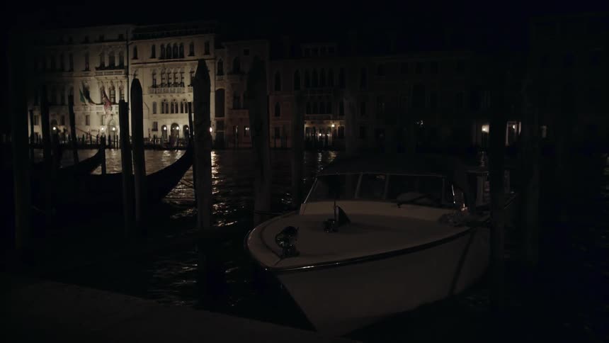 A boat bobs in a water way while tied to a pier at night