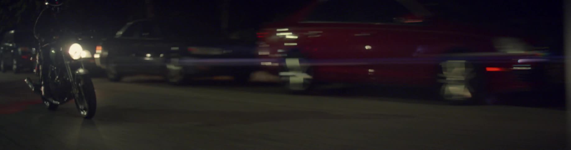 A row of cars race by as a motorcycle passes