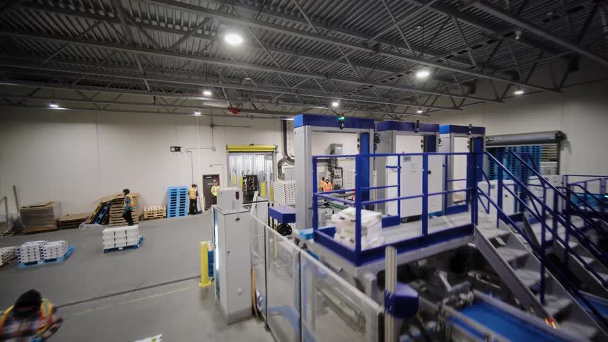 A rising high-angle shot reveals the operations of a busy food packaging warehouse with workers and conveyor belts