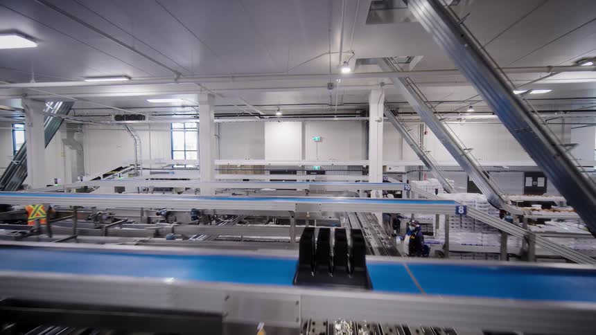 An aerial tracking shot reveals the complex, automated conveyor belt systems of a large food processing plant