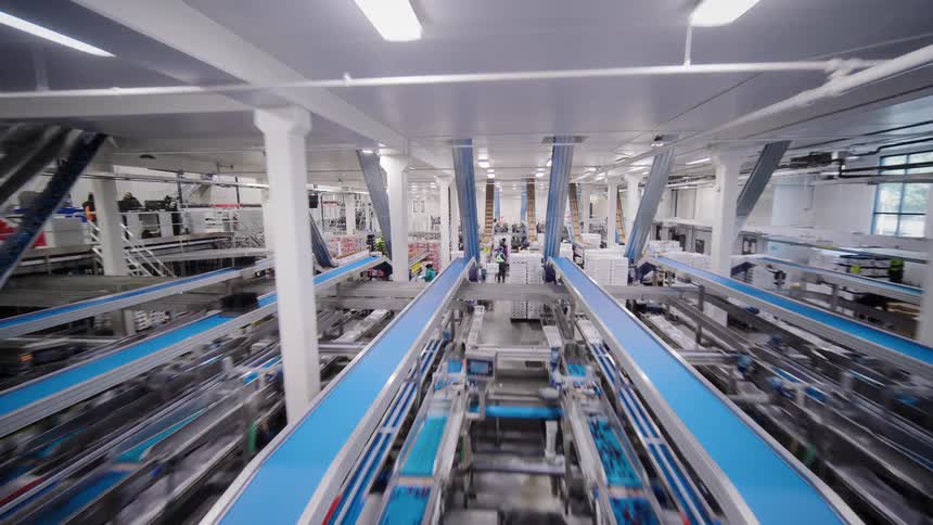 A sweeping drone shot flies through a large, modern, and automated food packaging factory with workers busy on the assembly line