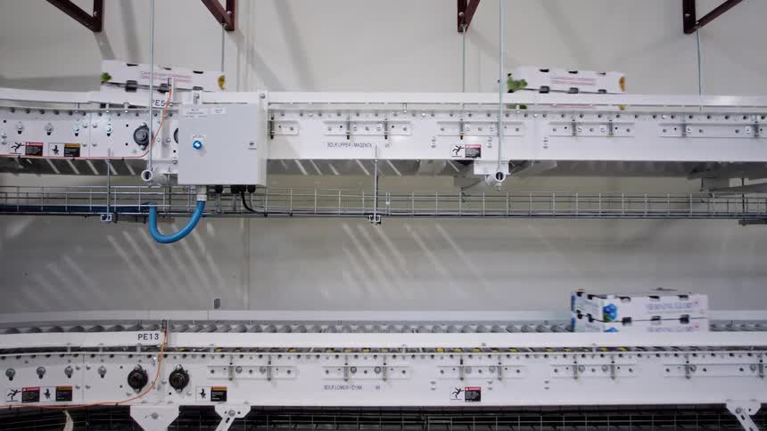 White boxes travel on a two-tiered automated sorting and conveyor system inside a modern factory