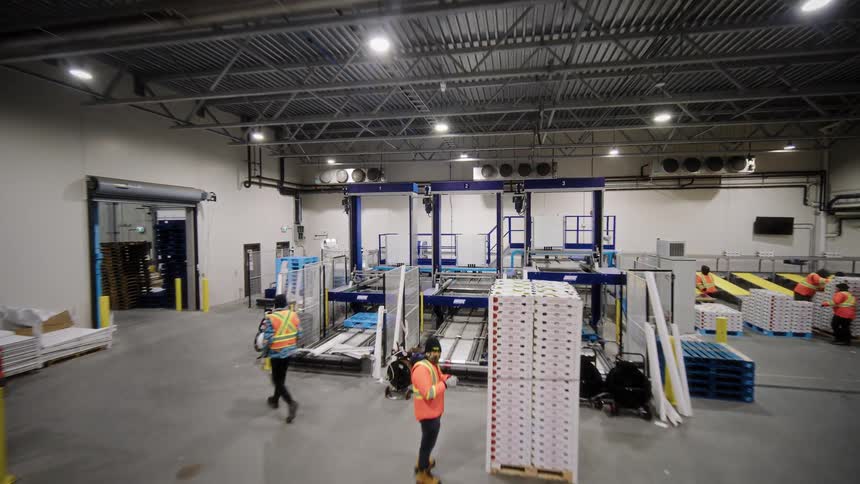 Tracking shot moving through a modern food packaging warehouse, revealing workers, forklifts, and complex automated machinery