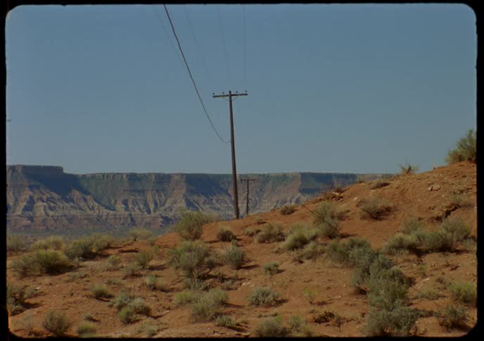 A vintage film shot captures a solitary telephone pole against a vast desert canyon landscape