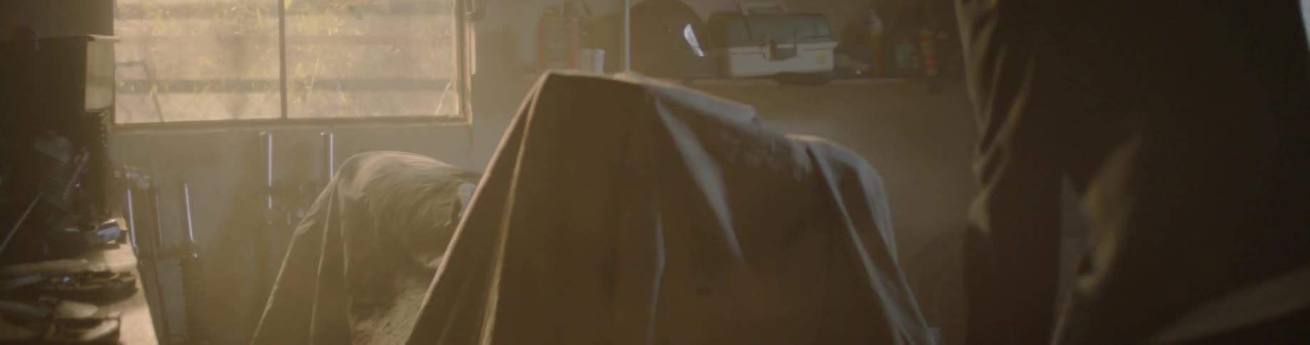 A person walks in his garage and removes a tarp from a motorcycle