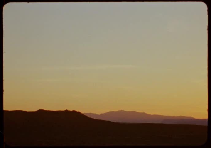Vintage footage captures a serene desert landscape with silhouetted mountains against a beautiful sunset sky